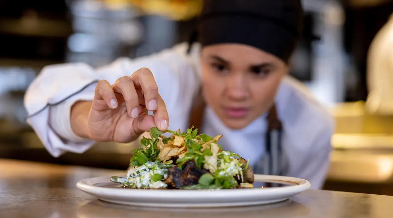 A chef adding a finishing detail to a plated entree